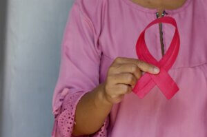 Woman in pink dress holding pink ribbon that symbolises breast cancer 